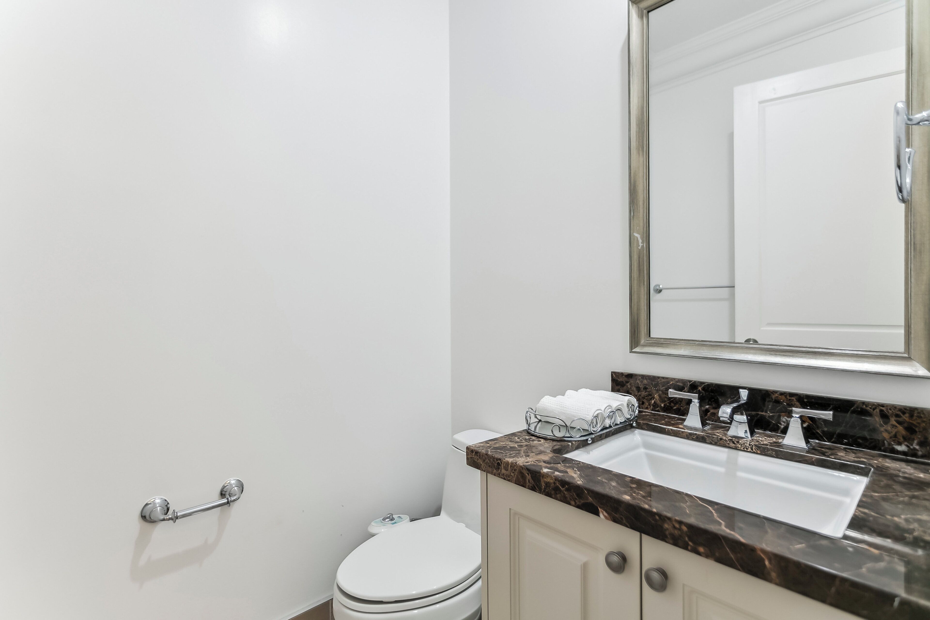 Un baño con inodoro blanco, lavamanos de mármol y un espejo grande.
