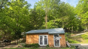 A small wooden cabin with a metal roof, surrounded by lush green trees. - Spotted Sandpiper - Cabin #3 (Trumansburg)