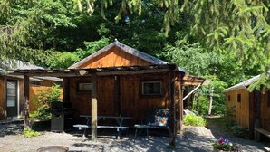 A rustic cabin with a wooden exterior, a porch with benches, and a small outdoor seating area. - Spotted Sandpiper - Cabin #3 (Trumansburg)