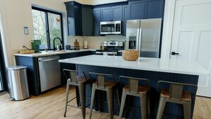 Una cucina moderna con pensili blu scuro, un piano di lavoro bianco, elettrodomestici in acciaio inossidabile e tre sgabelli da bar.