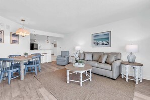 A modern living room with a grey sofa, a coffee table, and a dining area with blue chairs.