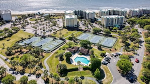 Een luchtbeeld van een resort met meerdere gebouwen, een strand, tennisbanen en een zwembad.