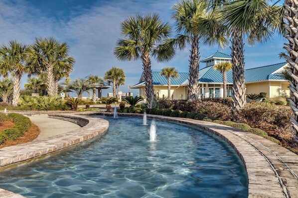 A pool with clear water, surrounded by palm trees and a building with a blue roof. - Stunning Litchfield 2BR Condo at Seaside Inn (Pawleys Island)