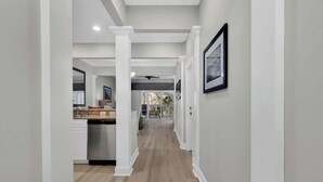 A hallway with a kitchen area, white walls, and wooden flooring.