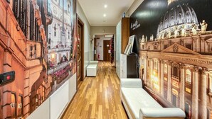 A hotel corridor with wooden flooring, a white bench, and a mural of a classical building. - B&B Le Suite di Via Catone (Rome)