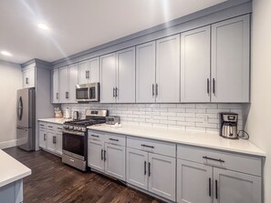 A modern kitchen with grey cabinets, stainless steel appliances, and a white tiled backsplash. - Roof Deck, Sleeps 10, W/D, Waterviews! (Boston)