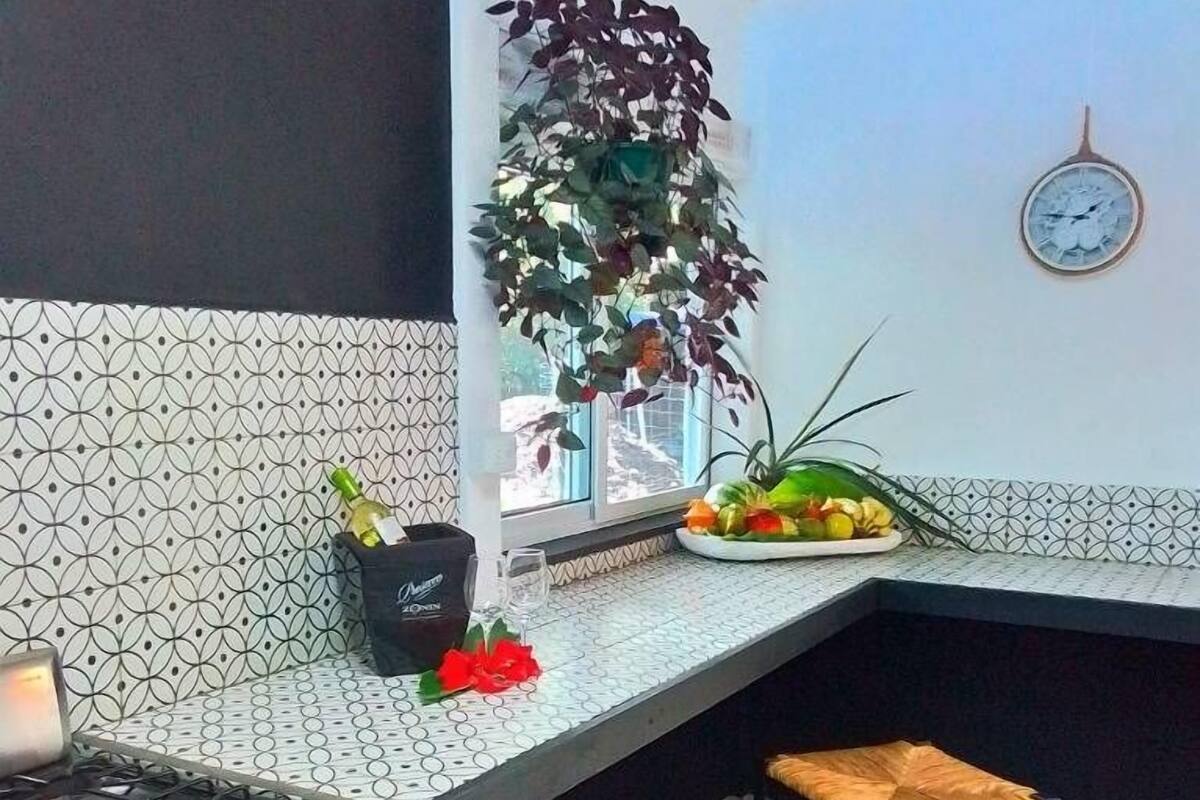 A kitchen with a gas stove, two stools, a potted plant, and a clock on the wall.
