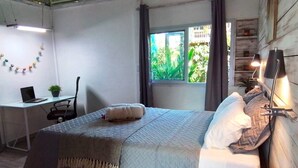 A bedroom with a bed, a desk, a chair, a window with curtains, and a plant. - Casitas en la Jungla - Luz Tropical (Puerto Viejo de Talamanca)