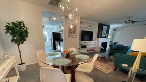 Ein modernes Wohnzimmer mit einem Glastisch, weißen Stühlen, einem grünen Sofa und einem Deckenventilator.