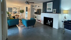 Ein modernes Wohnzimmer mit Kamin, blauen Sofas und einem Essbereich im Hintergrund.