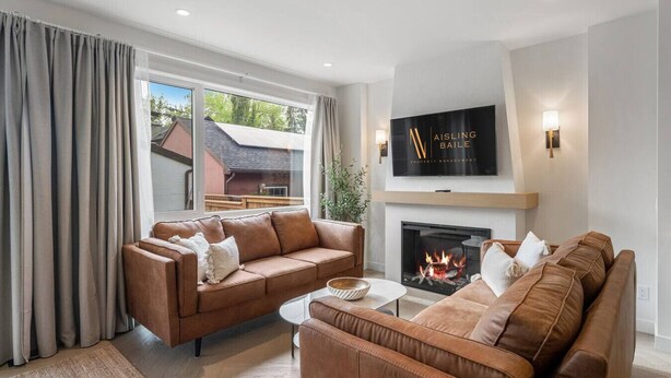 A modern living room with two brown leather sofas, a glass coffee table, and a fireplace. - La Maison | Pvt Hot Tub | Kensington | 2500 sqft (Calgary)