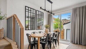 A modern dining area with a wooden table and black chairs, a staircase with wooden steps, and a large window with a view of the outside. - La Maison | Pvt Hot Tub | Kensington | 2500 sqft (Calgary)