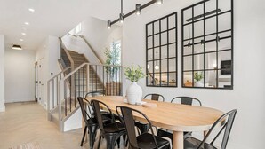 A modern dining area with a wooden table, black chairs, and a large window with a grid pattern. - La Maison | Pvt Hot Tub | Kensington | 2500 sqft (Calgary)