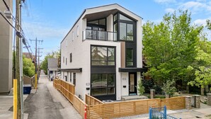 A modern two-story residential building with large windows, a balcony, and a fenced front yard. - La Maison | Pvt Hot Tub | Kensington | 2500 sqft (Calgary)