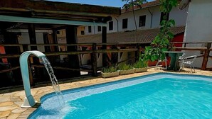 A swimming pool with a clear blue water feature, surrounded by a tiled deck and a wooden fence. - Pousada Sr Marinheiro Ubatuba (Ubatuba)