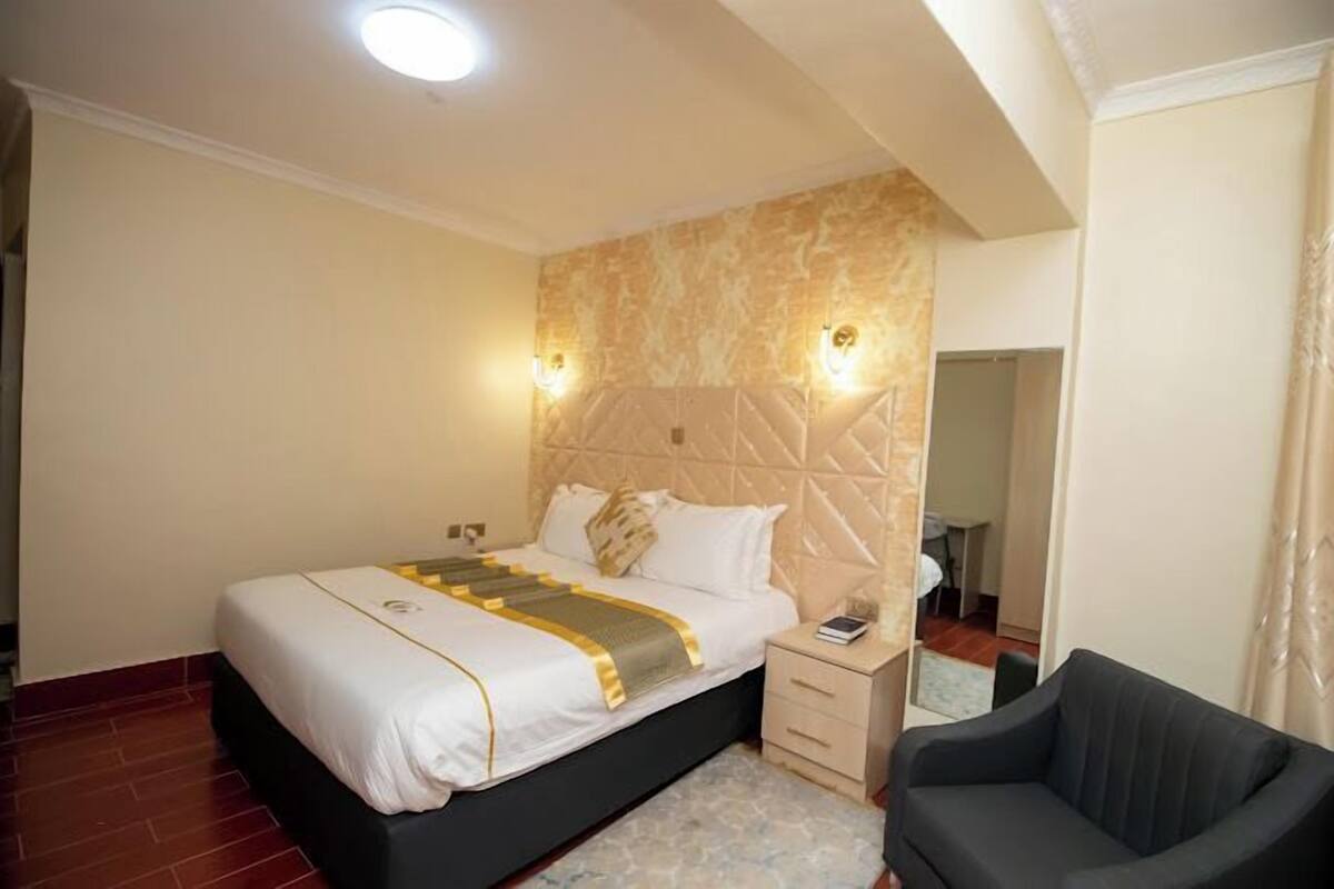 A hotel room with a bed, bedside table, and a chair.