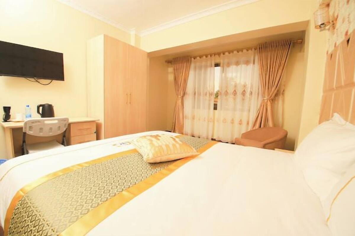 A hotel room with a bed, a desk with a chair, a television, and a window with curtains.