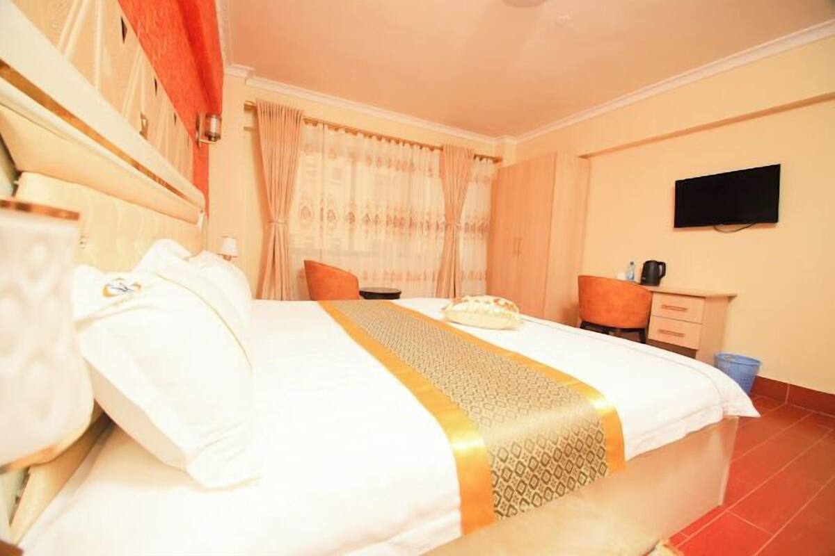 A hotel room with a bed, a desk, a chair, a television, and a window with curtains.