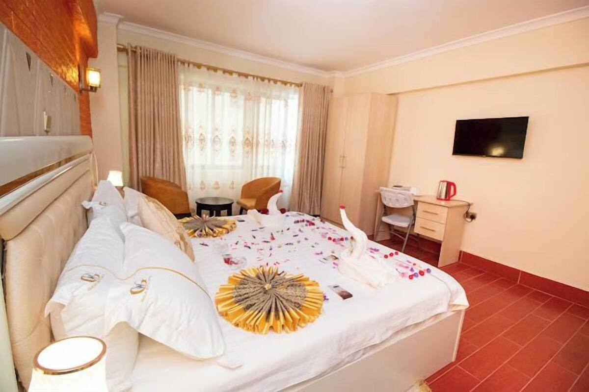 A hotel room with a large bed, a desk, a chair, a TV, and a window with curtains.