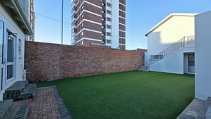 A courtyard with artificial grass, a brick wall, and a staircase leading to a white building.
