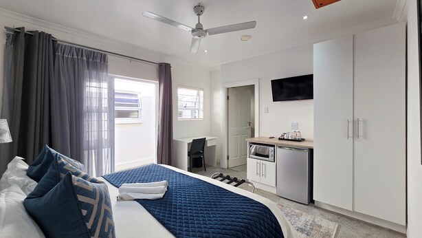 A hotel room with a bed, a desk, a kitchenette, and a TV.