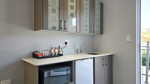 A compact kitchen with a built-in dishwasher, a stainless steel sink, and a small countertop with a kettle and condiments.