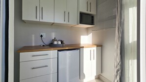 A compact kitchen with white cabinets, a wooden countertop, a built-in microwave, and a refrigerator.