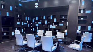 A conference room with a round table and white chairs, surrounded by dark walls with blue rectangular cutouts.