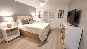 Ein Schlafzimmer mit Bett, Nachttischen, Deckenventilator, Fernseher und Kommode.