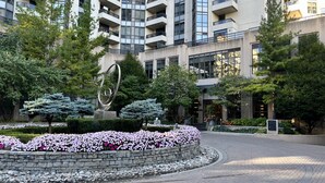 Un edificio moderno con una scultura centrale, circondato da giardini curati e alberi.