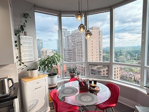 Une cuisine moderne avec une baie vitrée, une vue sur la ville et un coin repas avec des chaises rouges.
