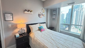 Una camera da letto con un letto, comodini, una mensola a parete con oggetti decorativi, un certificato incorniciato e una finestra vista città.