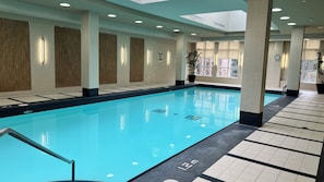 Une piscine intérieure à l’eau claire, entourée de murs et de colonnes recouverts de carreaux, et une horloge fixée au mur.
