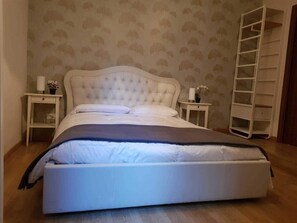 A bedroom with a tufted headboard bed, two bedside tables with lamps and flowers, and a wooden floor. - Bed&bicycle Guesthouse (Rome)