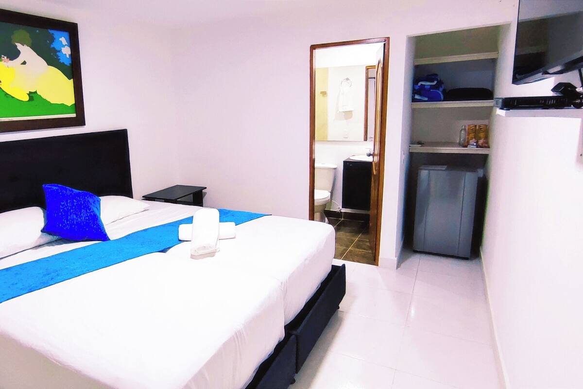 Una camera d'albergo con un letto, un comodino, una TV e una porta che dà su un bagno.