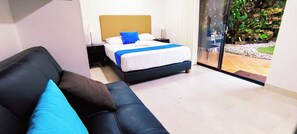 A hotel room with a bed, a black leather sofa, and a view of a garden through a glass door. - Hotel Campestre La Martina (Rionegro)