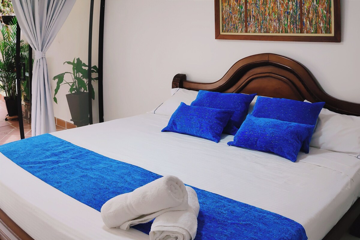 A neatly made bed with blue bedding and pillows, a white blanket, and a rolled white towel.