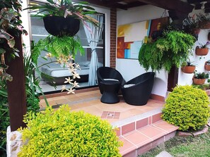 A covered patio area with a seating arrangement, potted plants, and a view of the interior through a glass door. - Hotel Campestre La Martina (Rionegro)