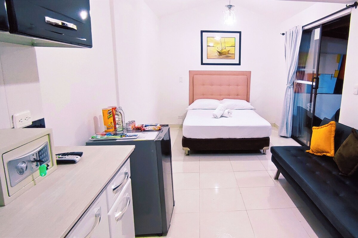 A hotel room with a bed, a sofa, a desk with a computer, a painting, and a window with curtains.