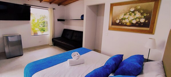 Habitación de hotel con cama, sofá, un cuadro, televisor y ventana con cortina.