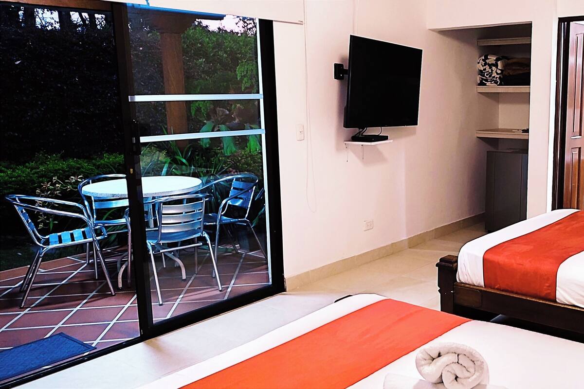 Camera d'albergo con due letti, una TV, un balcone con sedie e un tavolino.
