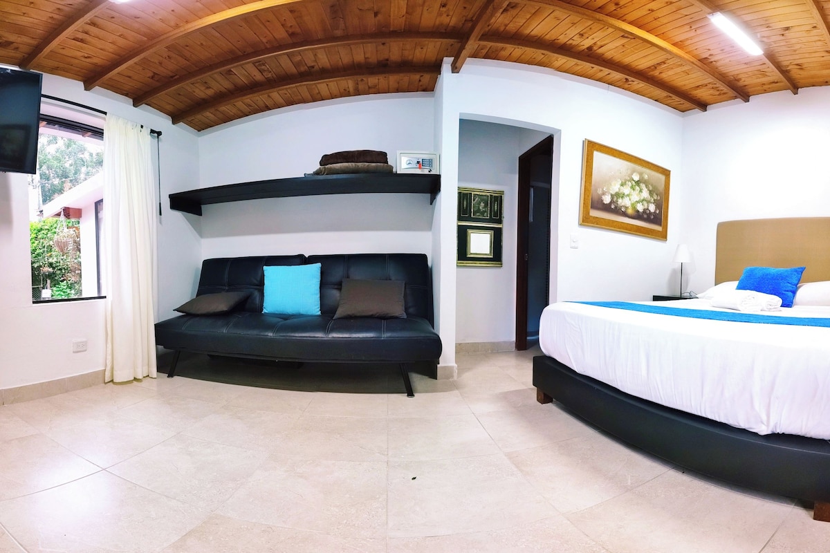 Een kamer met een zwarte bank, een bed met wit beddengoed, een houten plafond en een fotokader aan de muur.