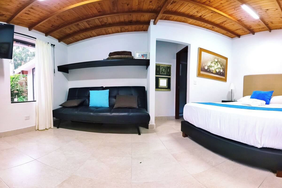 Una stanza con un divano nero, un letto con biancheria bianca, un soffitto in legno e un quadro appeso al muro.