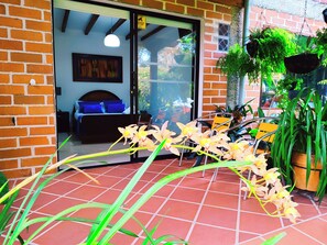 A patio area with a tiled floor, a bed with blue bedding, and hanging plants. - Hotel Campestre La Martina (Rionegro)