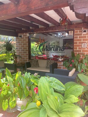 A cozy outdoor seating area with a large window, a wooden pergola, and lush green plants. - Hotel Campestre La Martina (Rionegro)