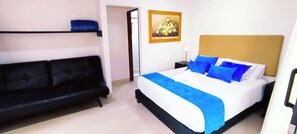 A bedroom with a bed, a black sofa, a nightstand with a lamp, and a painting on the wall. - Hotel Campestre La Martina (Rionegro)