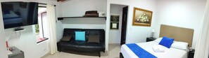 A hotel room with a bed, a sofa, a TV, and a painting on the wall. - Hotel Campestre La Martina (Rionegro)