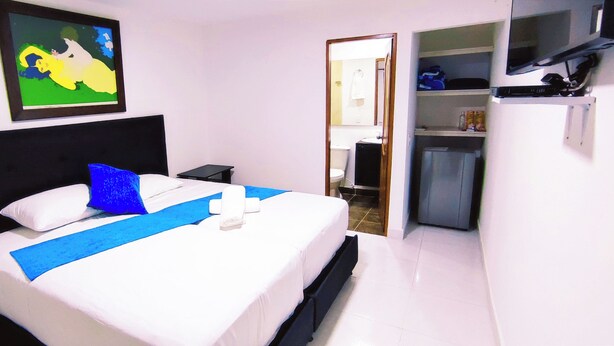 A hotel room with a bed, a nightstand, a TV, and a door leading to a bathroom. - Hotel Campestre La Martina (Rionegro)