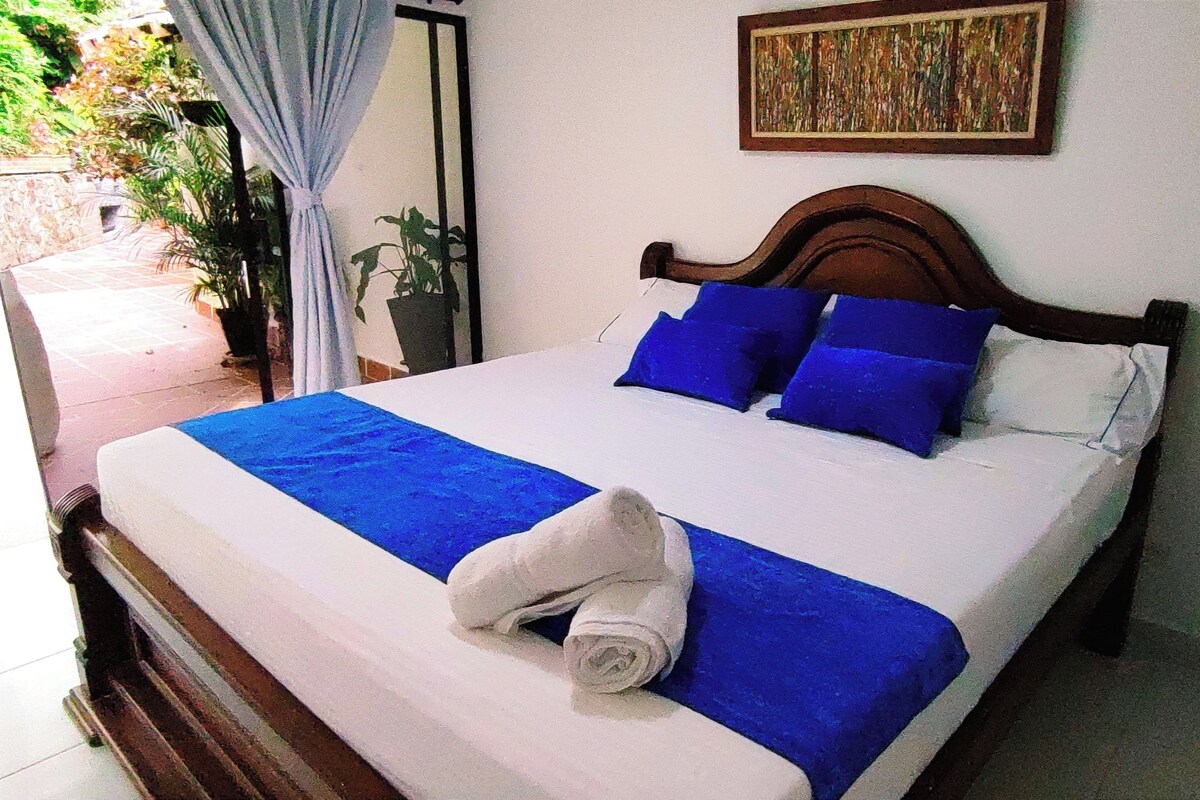 Un letto rifatto con cura, con biancheria azzurra e bianca, una testiera in legno e un asciugamano arrotolato sopra il letto.