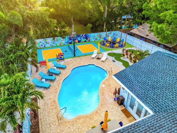 A swimming pool with blue lounge chairs, a basketball court, and a mural.